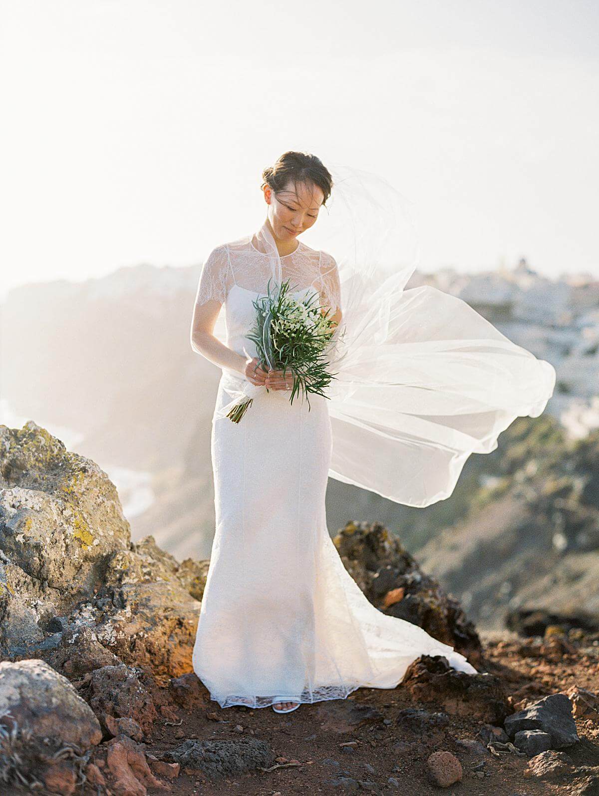 bride in white dress with long veil portrait at a santorini wedding at a cliff at santorini