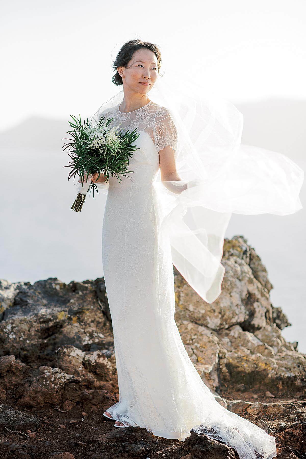 bride in white dress with long veil portrait at a santorini wedding at a cliff at santorini