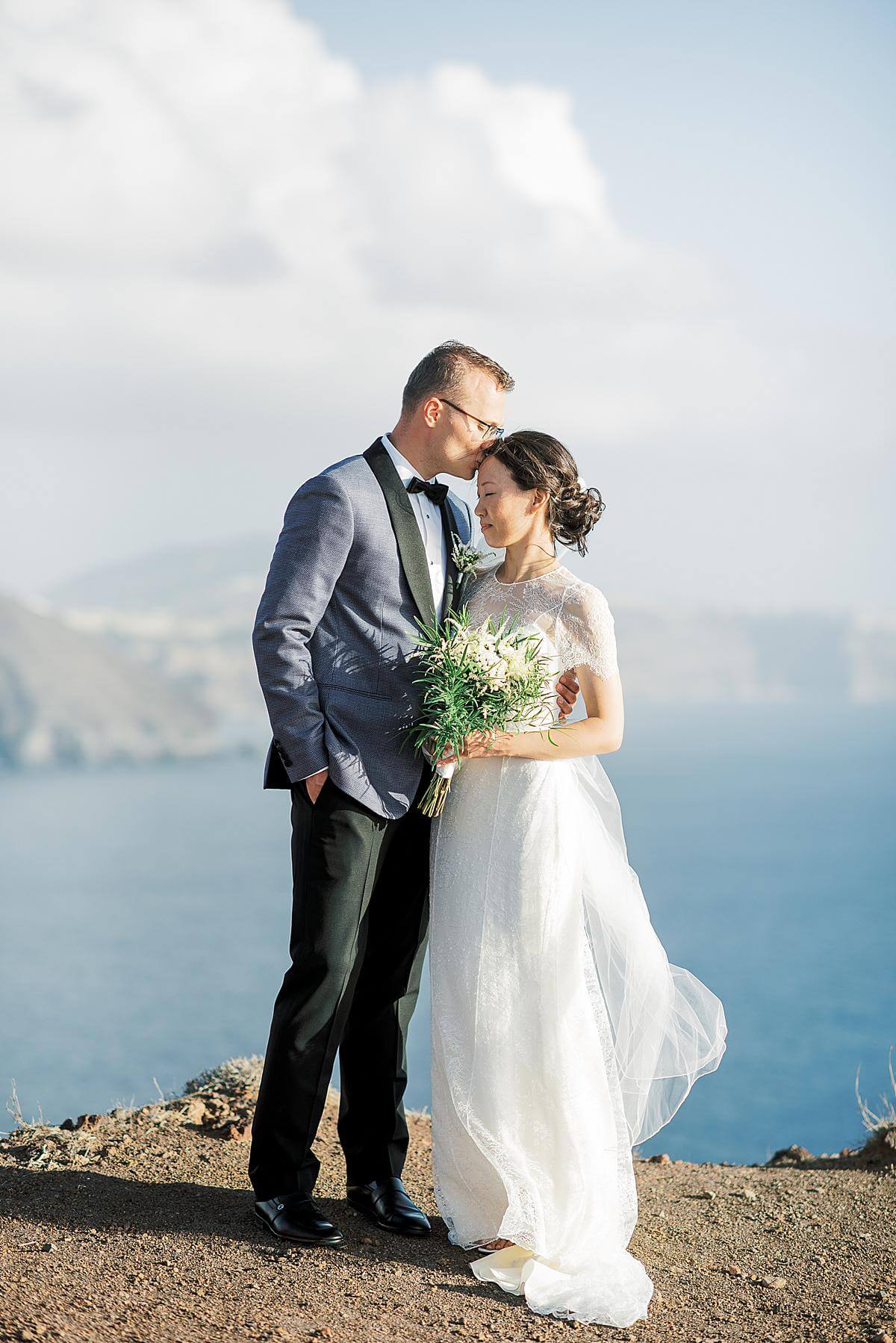 groom kissing bride at santorini wedding overlooking cliffs