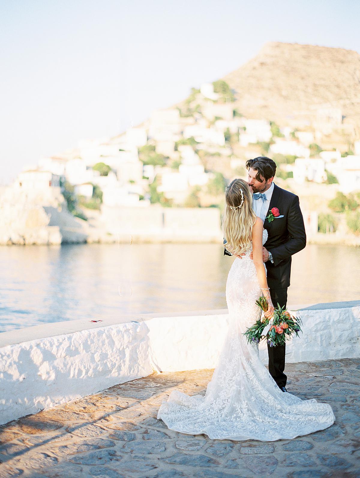 groom embracing bride at sunset restaurant venue on Hydra island_2