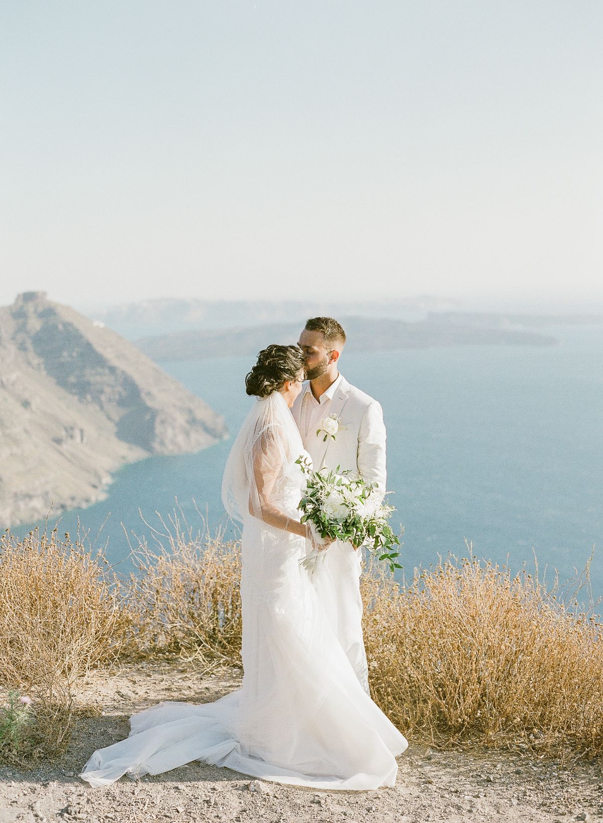 elopement in santorini - wedding photographer greece - couple being photographed on the edge of a cliff